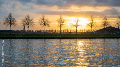 Reflection on the water of the Amsterdam-Rijn Kanaal in the Netherlands during sunset, with a silhouet of the Dutch town Schalkwijk on the other side of the canal.