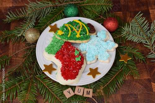 Iced holiday short bread cookies, tree, snowflake and stocking on white plate with stars and glitter ornaments. 