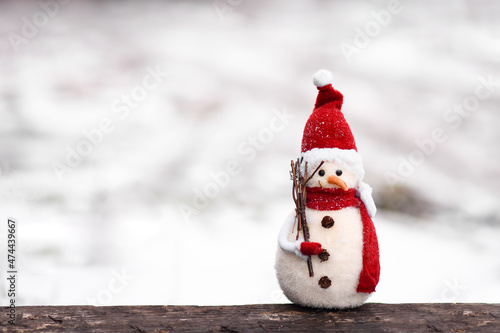 Photography a small snowman toy in a red hat and scarf on a background of white snow