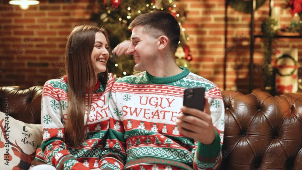 Attractive Man and Woman Talking by Video Call Sending Positive Emotions Looking at Camera. Happy Couple Sitting at Home while Recording Christmas Greetings. Happy New Year. Merry Christmas. Attractive Man and Woman Talking by Video Call Sending Positive Emotions Looking at Camera. Happy Couple Sitting at Home while Recording Christmas Greetings. Happy New Year. Merry Christmas.