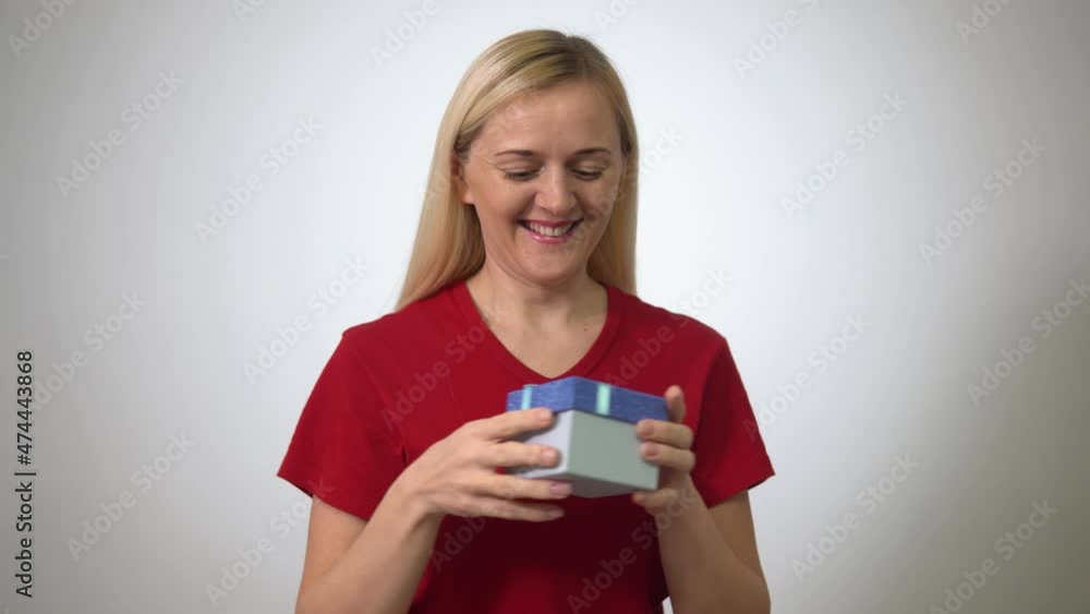 a blonde woman in a red T-shirt receives a box with a gift and is very surprised. a blonde woman in a red T-shirt receives a box with a gift and is very surprised.