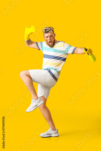 Dirty young man with cleaning sponge and detergent on yellow background