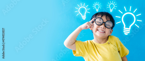 Smart kid nerd asian boy child with light bulb have good idea.Happy student kid thinking creative on blue banner background.Brainstorming and idea concept.online learning imagination innovation.stem.