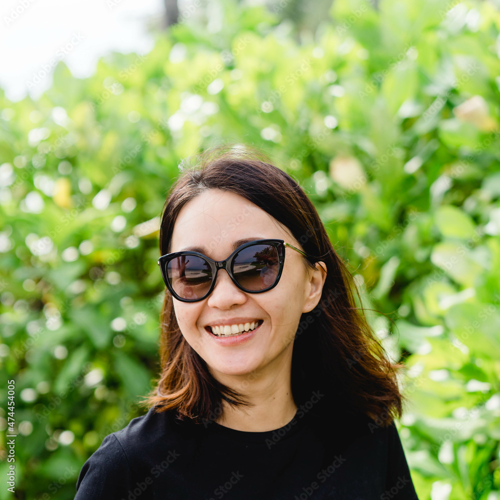 Asian style black hair model with sunglasses close up portrait outdoor nature background.Photo in motion of a smiling asian woman with black t shirt smile happy.Mental health care.good vacation travel Asian style black hair model with sunglasses close up portrait outdoor nature background.Photo in motion of a smiling asian woman with black t shirt smile happy.Mental health care.good vacation travel