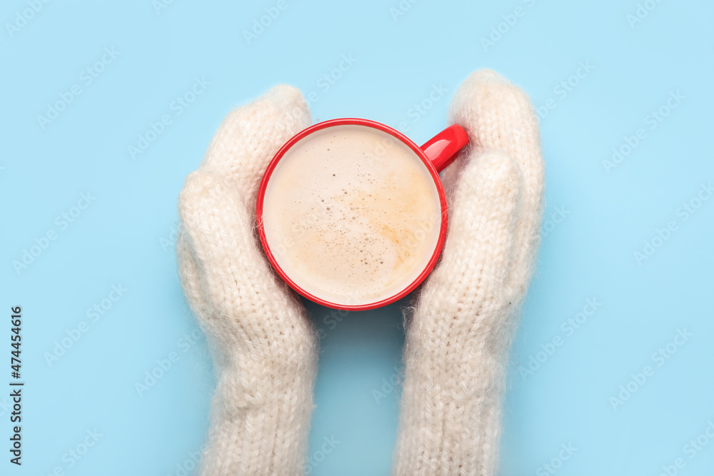 Female hands in knitted mittens and cup of tasty cacao on color background, closeup Female hands in knitted mittens and cup of tasty cacao on color background, closeup