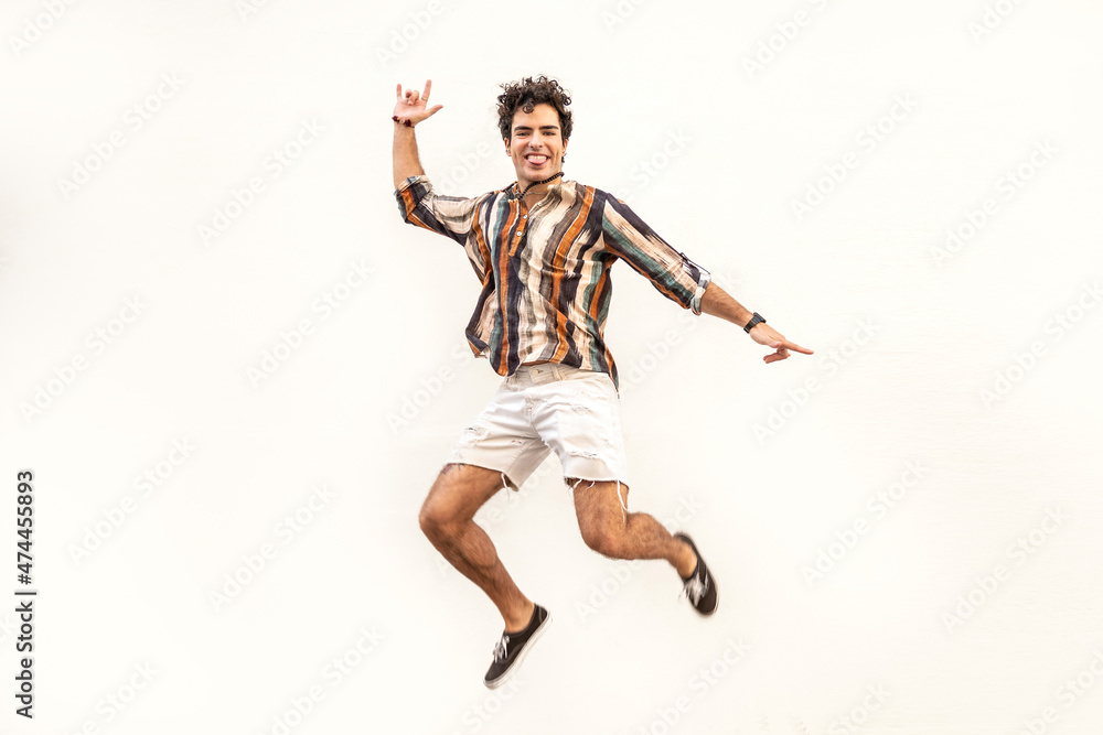 Handsome spanish man jumping over white wall. Funny face. Happiness. Real people emotions.