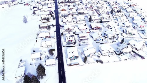 Aerial view of the rural snowy landscape in winter in Biberbrugg, Switzerland, the drone flying over the snow-covered houses, and the black asphalt road photo