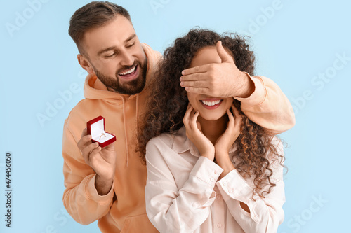 Young man proposing to his girlfriend on color background