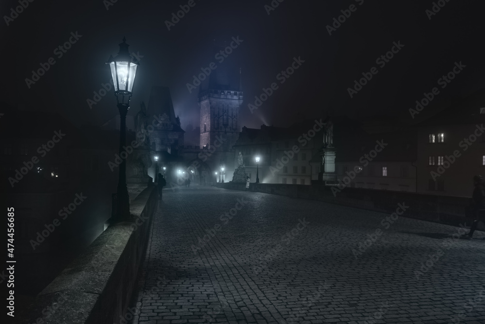 Street lamps and light from them on the old stone Charles Bridge in the night fog and silhouettes of figures