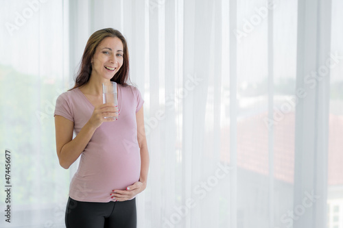 portraits of new moms european woman Russia is pregnant holding a glass of water by the window and smiling happily in the bedroom wearing a pink shirt and black pants Free Download portraits of new moms european woman Russia is pregnant holding a glass of water by the window and smiling happily in the bedroom wearing a pink shirt and black pants - GFXLoad