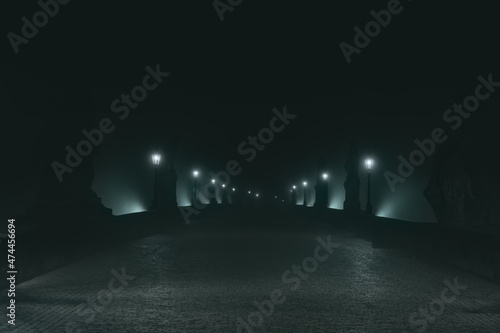 Street lamps and light from them on the old stone Charles Bridge in the night fog and silhouettes of figures