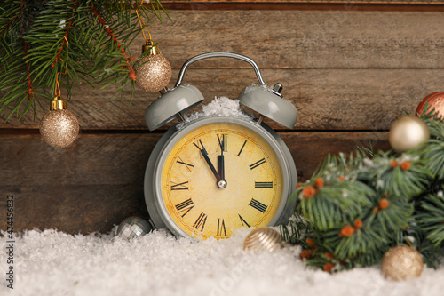 Christmas alarm clock and decorated fir branch on snow against wooden background