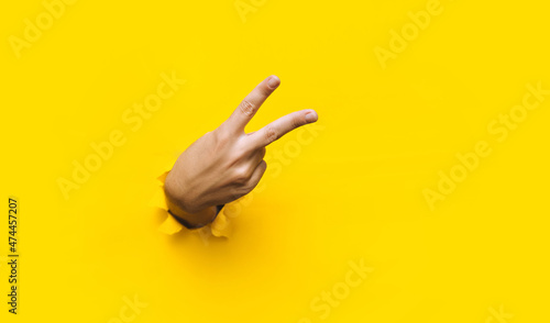 Victory sign two-finger hand gesture on yellow background with torn paper hole and copy space. It is ok concept. Backside.