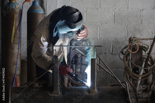 professional welder is welding metal frame and bright sparks in a workshop