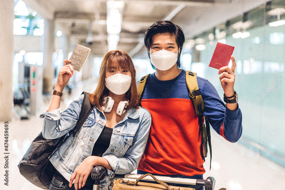 Young happy couple traveler in quarantine for coronavirus wearing surgical mask face protection hold passport and ticket before long travel vacation flight at International terminal airport
