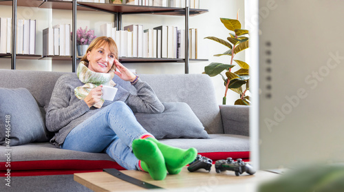 Senior caucasian woman sitting relaxingly on the sofa couch watching movie during winter time with warm cloth and scarf in her cozy home living room with copy space photo