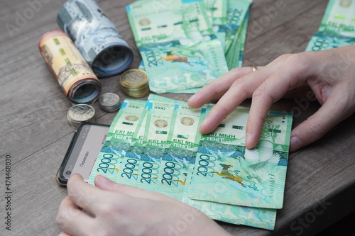 Almaty, Kazakhstan - 12.02.2021 : A man holds tenge bills in his hands against the background of a smartphone with mobile transfers