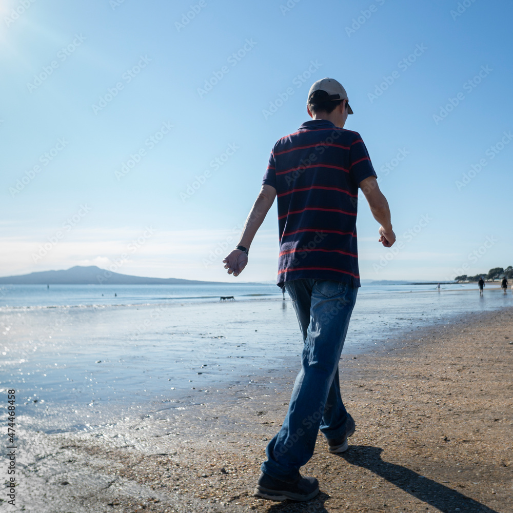 Man walking on the Milford beach with Rangitoto Island in the distance, Auckland. Vertical Format.