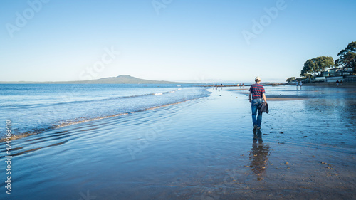 People walking on the wet sandy Milford beach with Rangitoto Island in the background, Auckland.