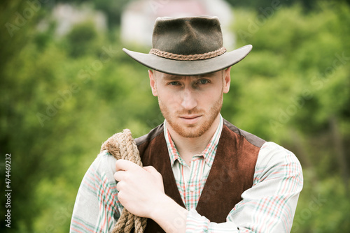Guy cowboy. Owner of ranch. Farm worker and farming concept. Cowboy with lasso rope on green background. Handsome man in cowboy hat and rustic style outfit.