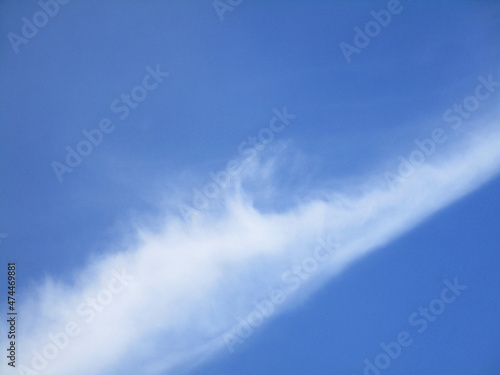 Blue sky with a diagonal white cloud resembling the crest of a sea wave, abstract background