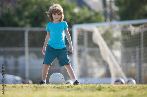 Excited child boy kicking ball in the grass outdoors. Soccer kids, children play football. Childhood and sport. Football little champion.