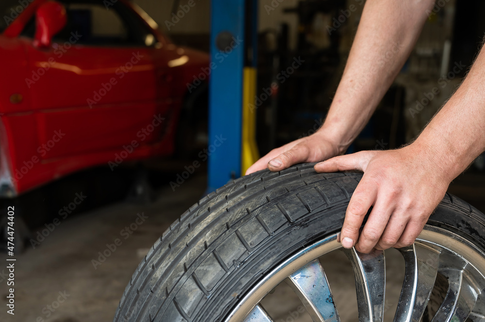 Fototapeta premium An auto mechanic holds a wheel of a car. Change of car tires according to the season