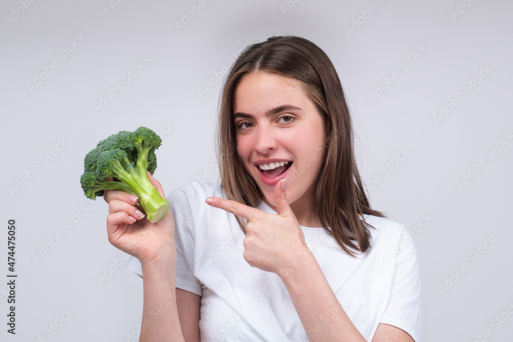 Woman showing broccoli. Healthy food, health life. Raw food concept. Womans hands holding bunch of broccoli over light gray background. Close up face, isolated with copy space. Woman showing broccoli. Healthy food, health life. Raw food concept. Womans hands holding bunch of broccoli over light gray background. Close up face, isolated with copy space.
