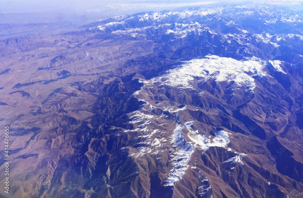 Snow-capped mountain peaks of the ridge. Northern snowy mountains. top view from the airplane window. Mountain landscape with snow-capped mountain peaks. Emerald mountain lakes and steep mountain