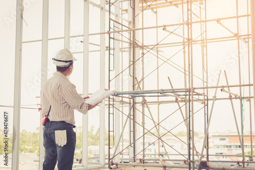 Engineer standing and looking home plans with white helmet at construction site.