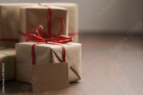 Brown paper gift boxes with red bow and blank paper card on walnut table with copy space