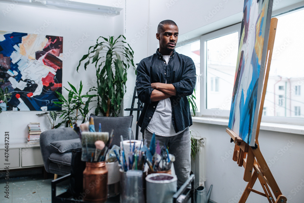 Critical black man looking at an easel with his unfinished painting
