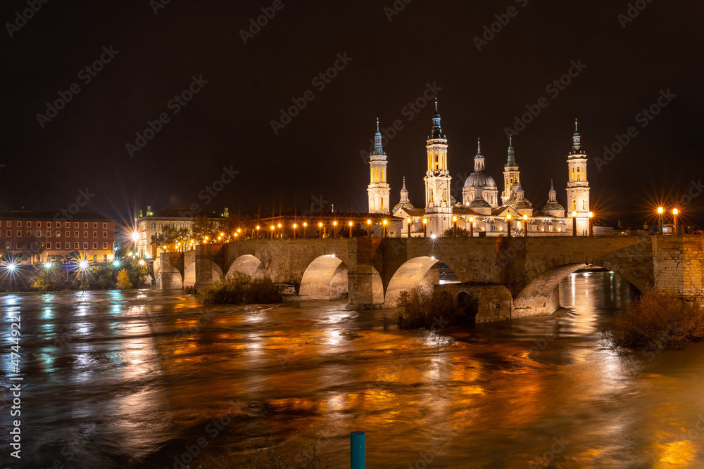 Naklejka premium Panoramic at night on the Puente de Piedra next to the Basilica of Nuestra Señora del Pilar on the Ebro river in the city of Zaragoza, Aragon. Spain