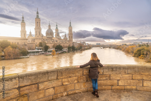 A young woman at sunset on the Stone Bridge next to the Basilica De Nuestra Señora del Pilar on the Ebro river in the city of Zaragoza, Aragon. Spain