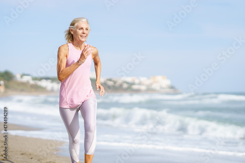 Fotografie Mature woman running along the shore of the beach