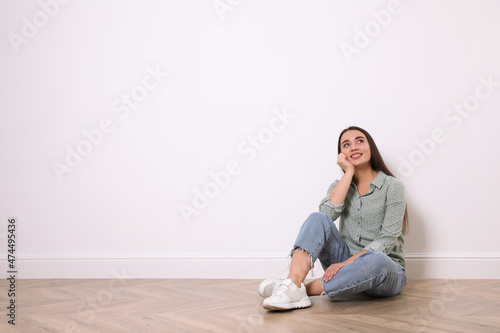 Young woman sitting on floor near white wall indoors. Space for text