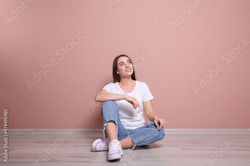 Young woman sitting on floor near pink wall indoors © New Africa