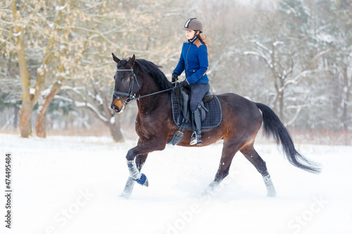 Young rider woman ejoying horse riding in winter park.
