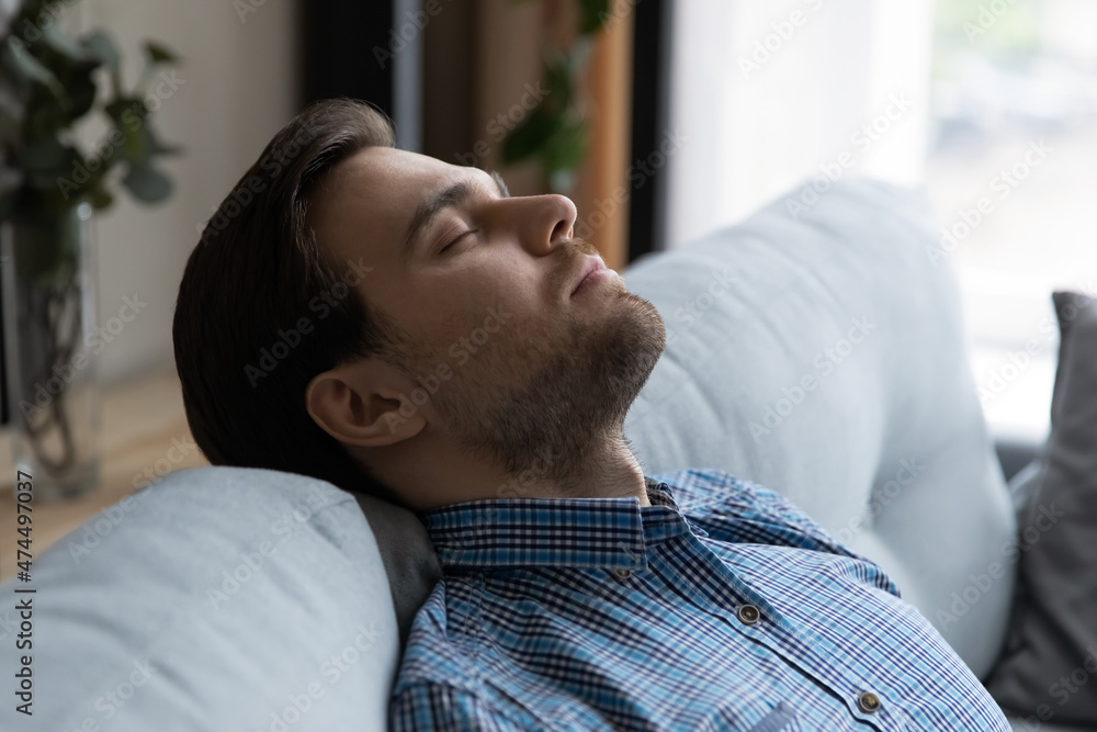 Close up handsome man falls asleep on sofa, put head on soft couch closed eyes breath fresh conditioned air inside modern living room or hotel relaxing indoor. Fatigue relief, climate control concept Close up handsome man falls asleep on sofa, put head on soft couch closed eyes breath fresh conditioned air inside modern living room or hotel relaxing indoor. Fatigue relief, climate control concept