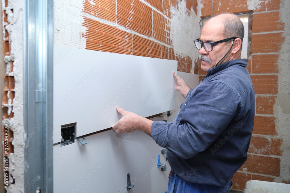 Senior constructor worker laying white ceramic tiles on the wall. Senior constructor worker laying white ceramic tiles on the wall.