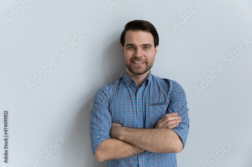 Attractive millennial guy wear casual blue shirt posing on gray wall studio background, single man portrait, crossed arms on chest smiling looking at camera advertise dental services clinic concept