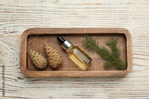 Tray with bottle of essential oil, fir branch and cones on white wooden table, top view