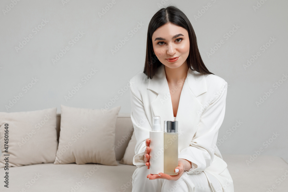 Young cosmetologist sitting on a white sofa in a studio with cosmetics on a white sofa Young cosmetologist sitting on a white sofa in a studio with cosmetics on a white sofa