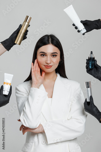 Good looking female cosmetologist posing in a studio with hands in black gloves holding cosmetic products around her
