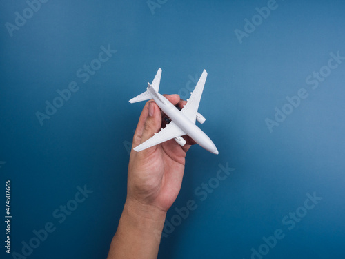 Hand holding white plane toy model on a blue background, top view, minimal style. White airplane, flat lay design. Flight, travel concept.