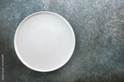 Empty white plate on a gray-blue background sprinkled with powder.
