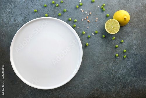 Empty white plate, green peas, lemon and Himalayan salt on a gray-blue background.