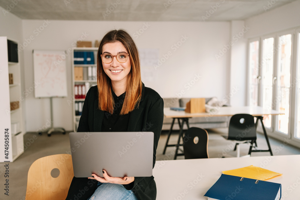 Friendly young businesswoman perched on the edge of office table Friendly young businesswoman perched on the edge of office table