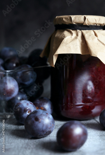 Jar of plum jam with fresh plums on gray background photo