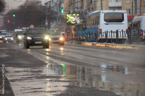 Cars on the road with puddles at snowy evening